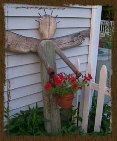 a wooden cross sitting on top of a white fence next to flowers and a potted plant