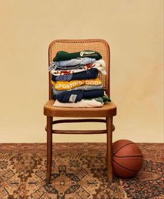 a stack of clothes sitting on top of a wooden chair next to a basketball