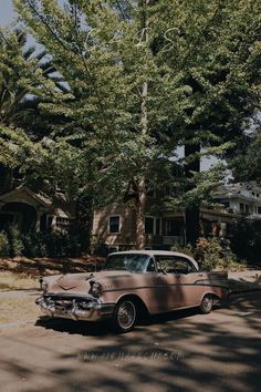 an old car is parked in front of a house with trees on the side walk