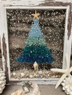 a christmas tree made out of sea glass in a frame with shells and starfish