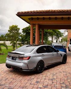 a silver car parked in front of a house next to two other cars on a brick driveway