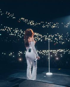 a woman standing on top of a stage next to a white pole with lights in the background