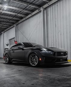 a black sports car is parked in a large garage with its hood up and lights on