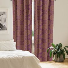 a bed sitting next to a window with purple curtains on top of it and a plant in the corner