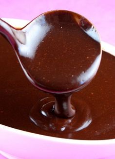 a spoon full of melted chocolate in a white bowl on a pink tablecloth,