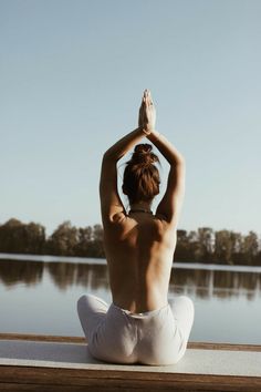 a person sitting on a dock doing yoga exercises with their hands up in the air