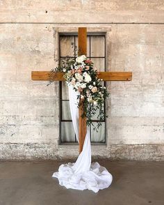 a cross decorated with flowers and greenery in front of a window at a wedding