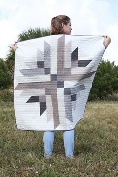 a woman holding up a quilt in the grass