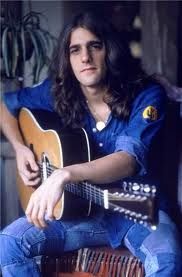 a man with long hair sitting and playing an acoustic guitar