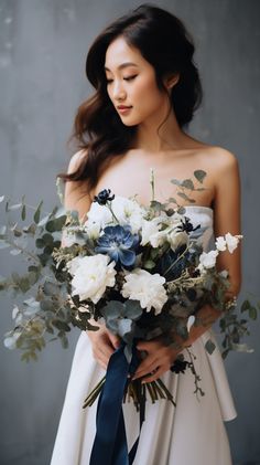 a woman in a white dress holding a bouquet of blue and white flowers with greenery