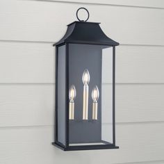 an outdoor light hanging from the side of a house with three candles lit up on it