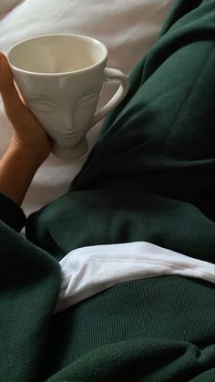 a person laying in bed holding a white cup with their hands on top of it