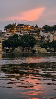 the sun is setting over an old town on top of a hill by the water