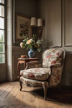 A cozy corner featuring French Country Décor, with a floral-patterned armchair, a small wooden side table, and a vase of fresh flowers in a blue and white porcelain vase. Small Apartment French Style, French Small Apartment, Distressed Wood Coffee Table, Warm Living Room Colors, Ideas For Small Apartments, New House Living Room, French Apartment