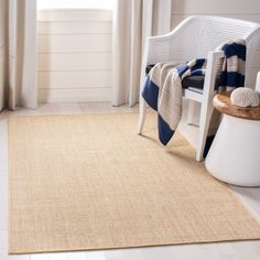 a white chair sitting in front of a window next to a rug on the floor