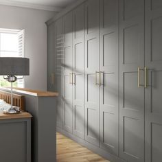 A run of grey wardrobes with shaker detailing and brass handles shown in a bedroom with wooden floors ad grey decor