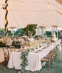 an outdoor tent with tables and chairs covered in white linens, greenery and candles