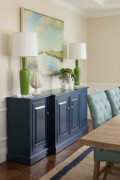 a dining room with blue cabinets and green vases on the sideboard in front of it