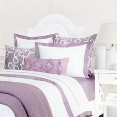 a bed with purple and white comforters in a bedroom next to a night stand