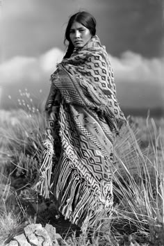 an old black and white photo of a woman wearing a shawl in a field