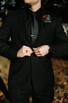 a man in a black suit and tie with his hands on his lapel button