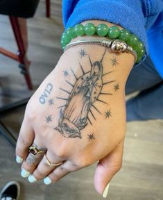 a woman's hand with a tattoo on it and a green beaded bracelet