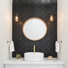 a white sink sitting under a round mirror on top of a counter next to two lights