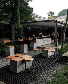 an outdoor bar with tables and stools in front of it, surrounded by greenery