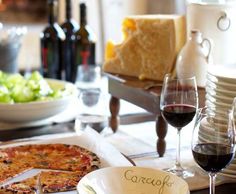 a table topped with plates and glasses of wine next to a pizza covered in cheese