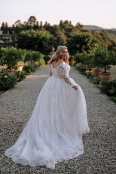 a woman in a wedding dress standing on gravel road