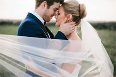 a bride and groom embracing each other with veil blowing in the wind over their heads