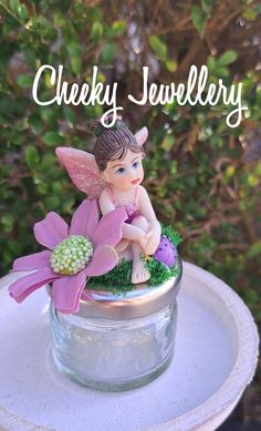 a small fairy figurine sitting on top of a glass jar filled with flowers