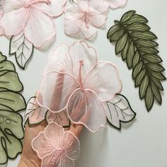 a person's hand is touching some pink flowers on a white surface with green leaves