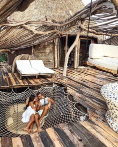 two people are sitting in a hammock on a wooden deck with thatched roof