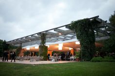 a group of people sitting at tables under an awning in the middle of a field