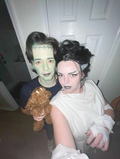 two people dressed up as zombies and one holding a teddy bear in front of a door