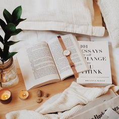 an open book sitting on top of a bed next to two candles and some books