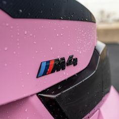 the rear end of a pink bmw car with rain drops on it's hood