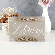 a wooden sign sitting on top of a table next to a vase filled with flowers