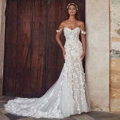 a woman standing in front of a wooden door wearing a wedding dress with flowers on it