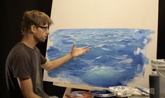 a man in glasses is holding his hand up to an easel and painting on a canvas