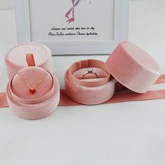 three pink velvet jewelry boxes with matching rings and necklaces in front of a framed photograph