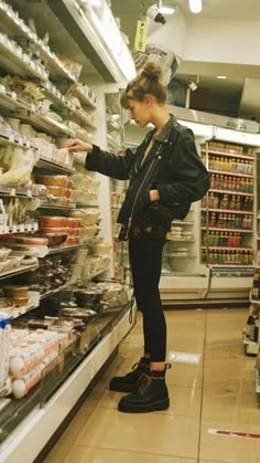 a woman standing in front of a display case at a grocery store looking for food