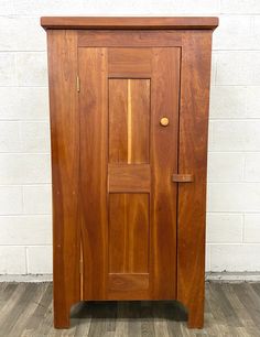 a wooden cabinet sitting on top of a hard wood floor next to a white brick wall