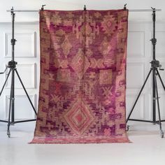 a pink and red rug hanging on a wall next to two tripod lights in front of a white door