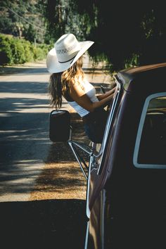 a woman sitting on the back of a car wearing a cowboy hat and leaning against it