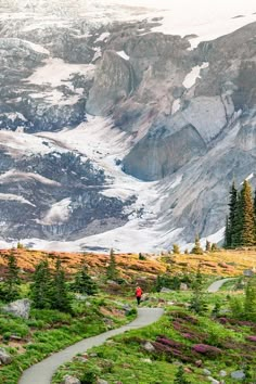 a person walking down a trail in the mountains with snow on the mountain behind them