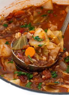 a ladle full of soup with vegetables and meats being held by a spoon