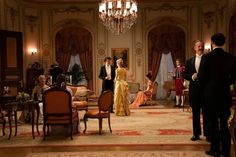 a group of people standing in a living room next to a chandelier and table