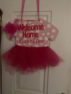 a welcome home sign hanging on the front door with a pink tutule skirt